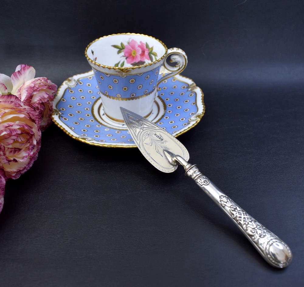A Victorian sterling silver pastry server with a pointed trowel-shaped blade engraved with floral motifs and an ornate relief handle. View IX