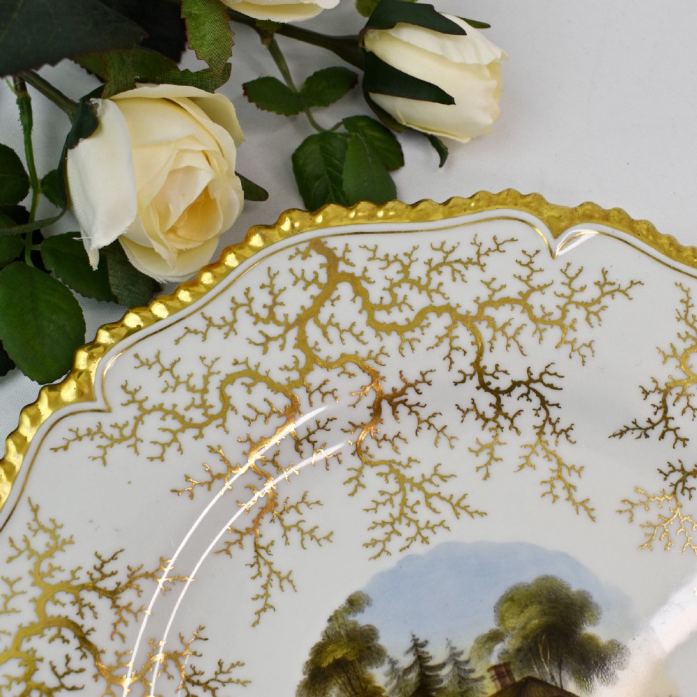 A Regency porcelain dessert plate featuring a hand-painted central landscape surrounded by intricate gold gilt seaweed patterns on a scalloped white border. View IV
