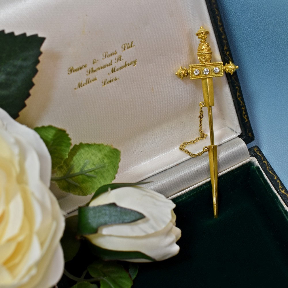 A Victorian 18 carat gold jabot pin crafted in the shape of a sword, featuring three old-cut diamonds set along the guard, cannetille wirework, and a safety chain. View II