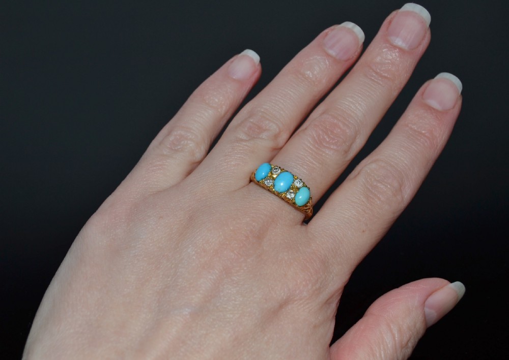 A Victorian 18ct gold ring featuring three oval turquoise cabochons separated by four accent diamonds in a carved band. View IX