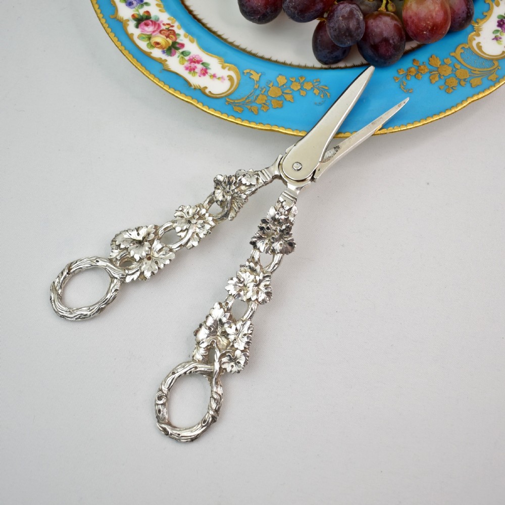 A pair of solid sterling silver grape scissors featuring heavily detailed cast grapevine handles with circular finger loops and tapered blades. View V