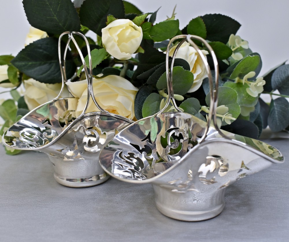 A pair of polished sterling silver bonbon baskets featuring pierced scrollwork patterns and high looped handles.