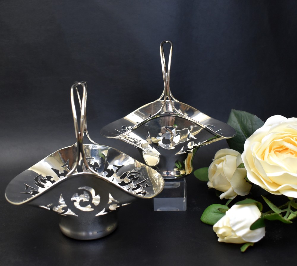 A pair of polished sterling silver bonbon baskets featuring pierced scrollwork patterns and high looped handles. View II
