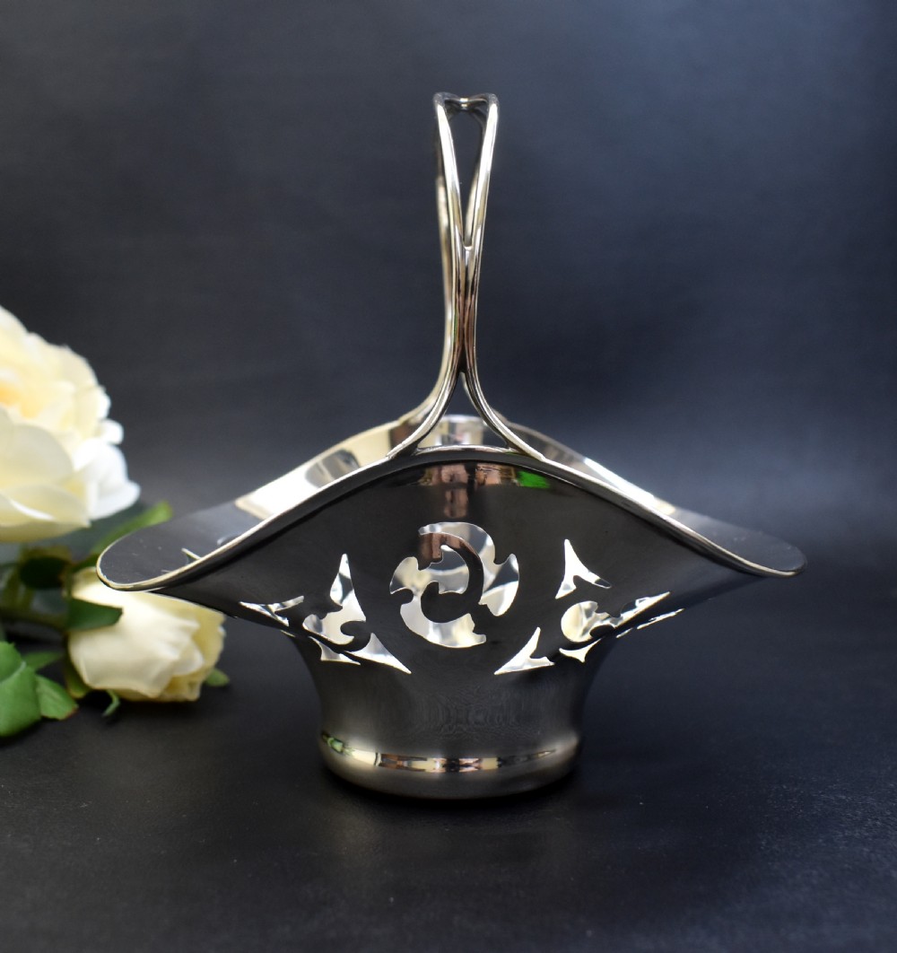 A pair of polished sterling silver bonbon baskets featuring pierced scrollwork patterns and high looped handles. View IV