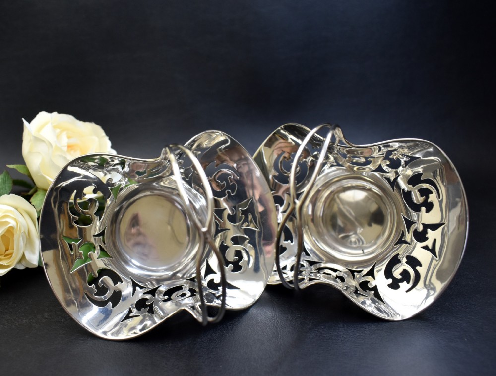 A pair of polished sterling silver bonbon baskets featuring pierced scrollwork patterns and high looped handles. View VI