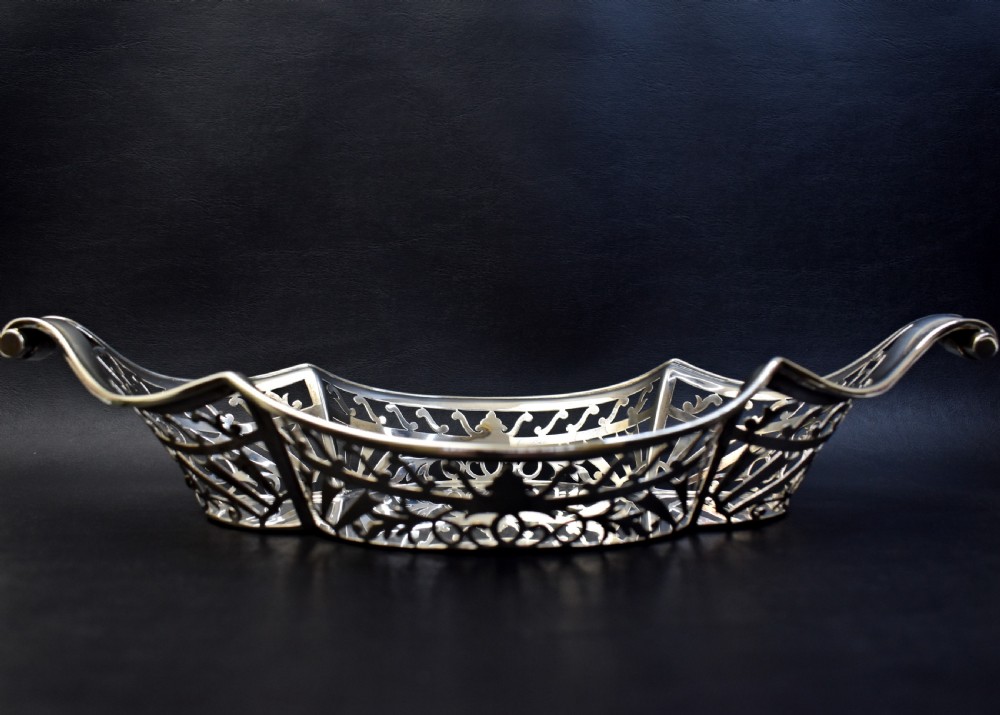 A sterling silver bread basket featuring pierced fretwork sides and swept scroll handles at both ends.
