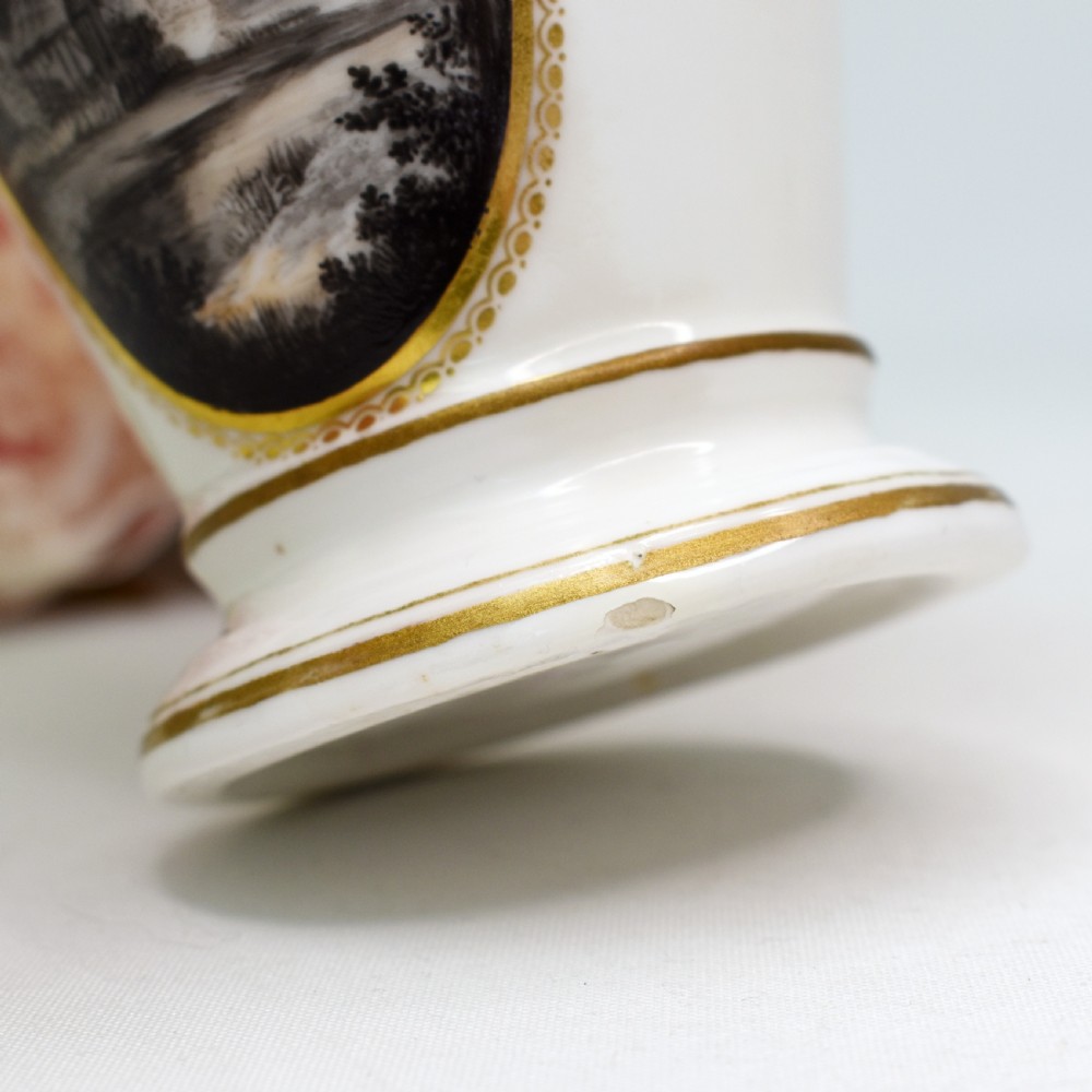 A white porcelain urn featuring two gilded scroll handles, a gilded rim with a vine motif, and an oval medallion painted with a monochrome landscape. View XI