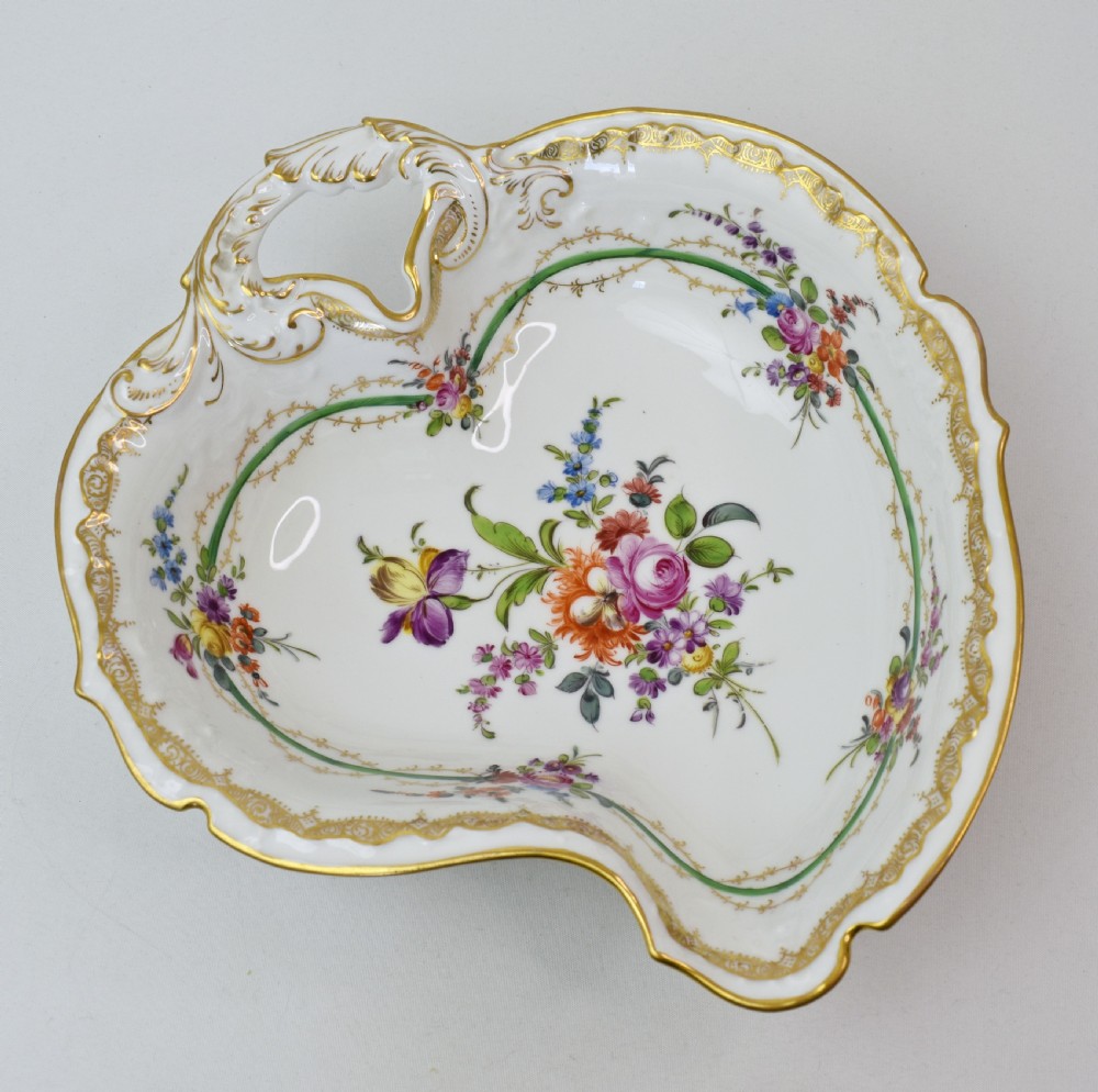 A white Rococo-style porcelain dish adorned with hand-painted floral sprays, a green inner rim, and a gilded scroll handle.