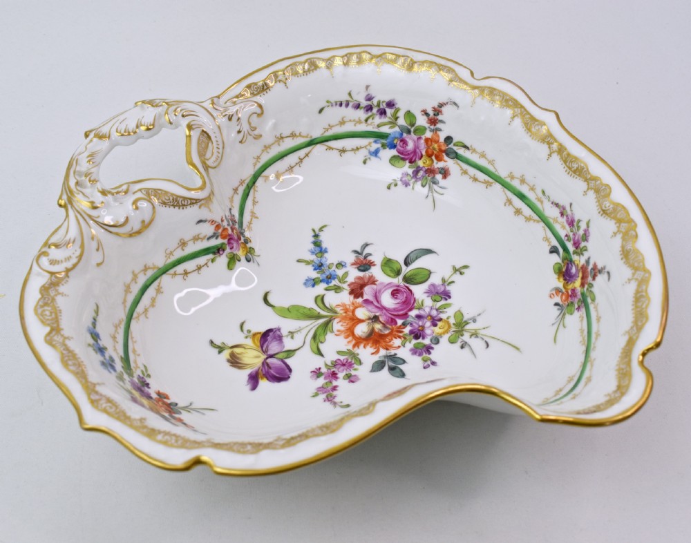 A white Rococo-style porcelain dish adorned with hand-painted floral sprays, a green inner rim, and a gilded scroll handle. View II