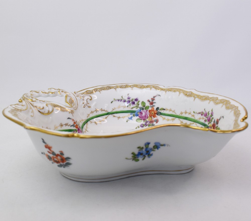 A white Rococo-style porcelain dish adorned with hand-painted floral sprays, a green inner rim, and a gilded scroll handle. View III