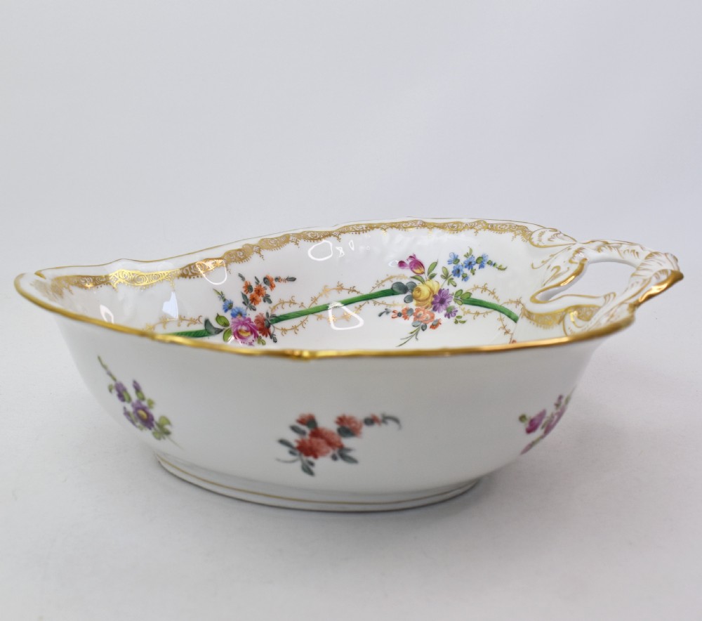 A white Rococo-style porcelain dish adorned with hand-painted floral sprays, a green inner rim, and a gilded scroll handle. View IV