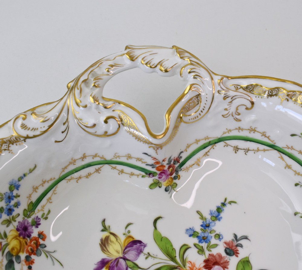 A white Rococo-style porcelain dish adorned with hand-painted floral sprays, a green inner rim, and a gilded scroll handle. View VI