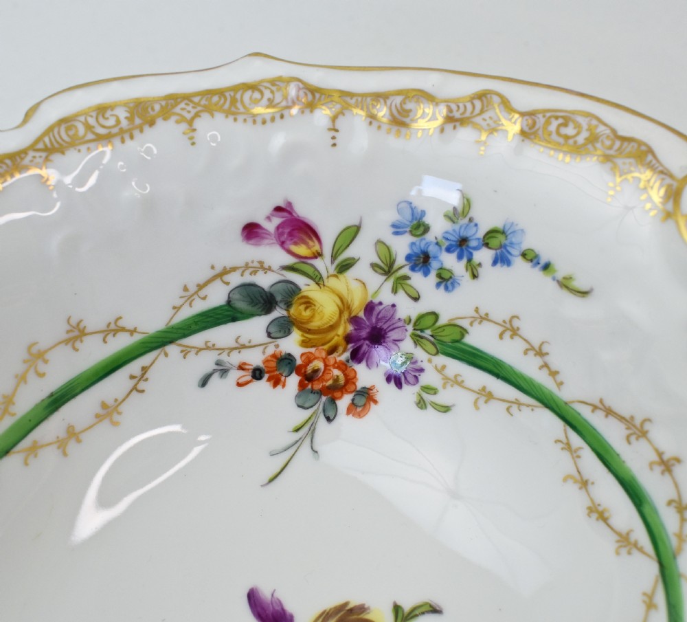 A white Rococo-style porcelain dish adorned with hand-painted floral sprays, a green inner rim, and a gilded scroll handle. View VII
