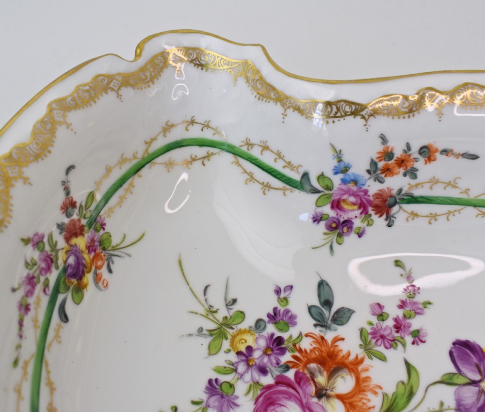 A white Rococo-style porcelain dish adorned with hand-painted floral sprays, a green inner rim, and a gilded scroll handle. View VIII
