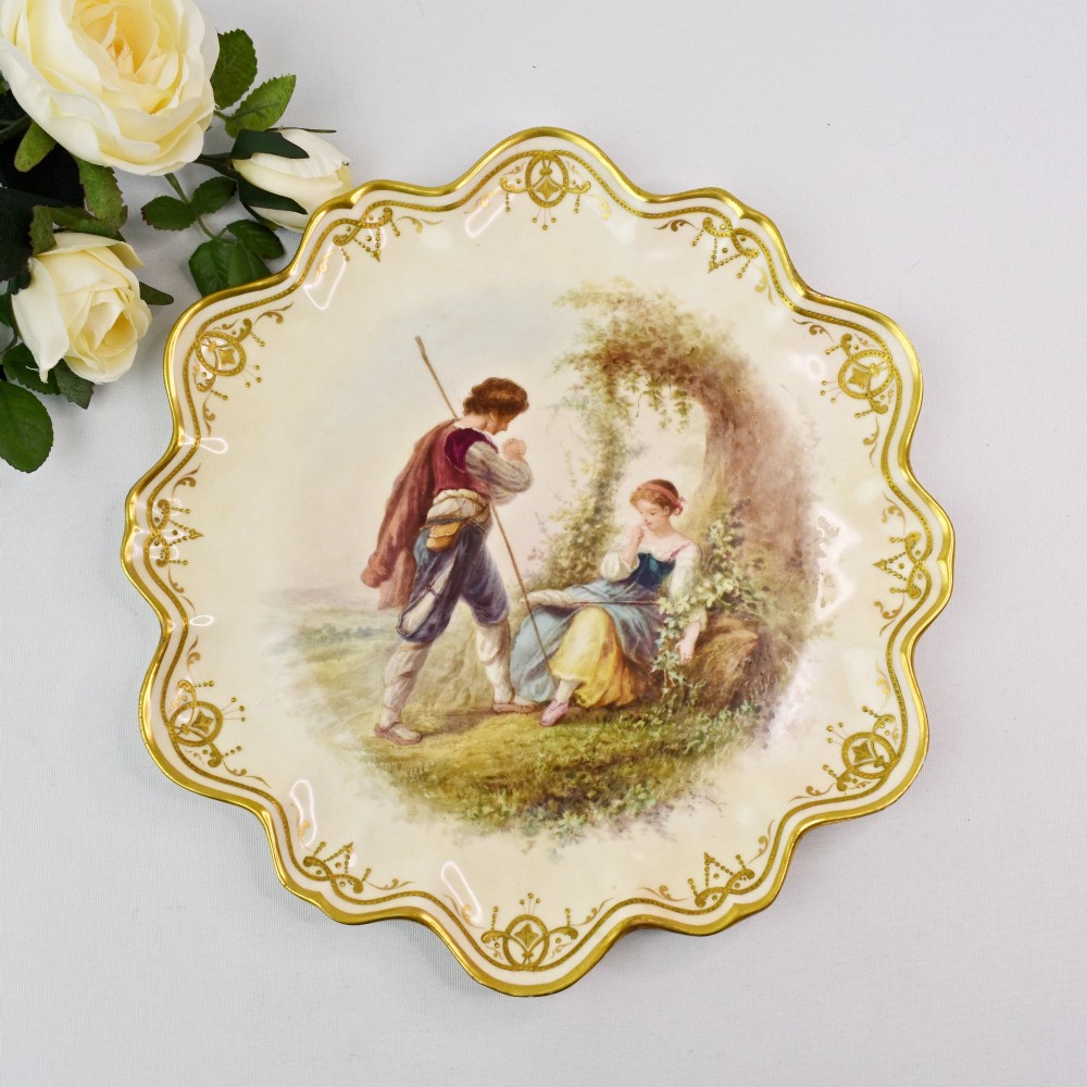 A circular Victorian porcelain cabinet plate featuring a hand-painted romantic pastoral scene enclosed by a lobed rim decorated with gold gilding. View II