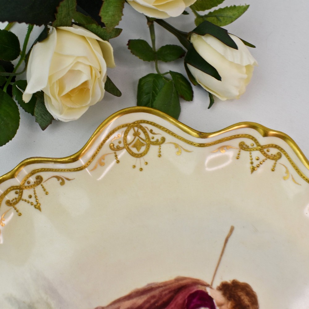 A circular Victorian porcelain cabinet plate featuring a hand-painted romantic pastoral scene enclosed by a lobed rim decorated with gold gilding. View VI