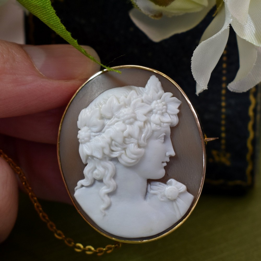 An oval Victorian shell cameo brooch depicting a relief profile carving of Antinous adorned with a floral wreath, set in a gold frame.