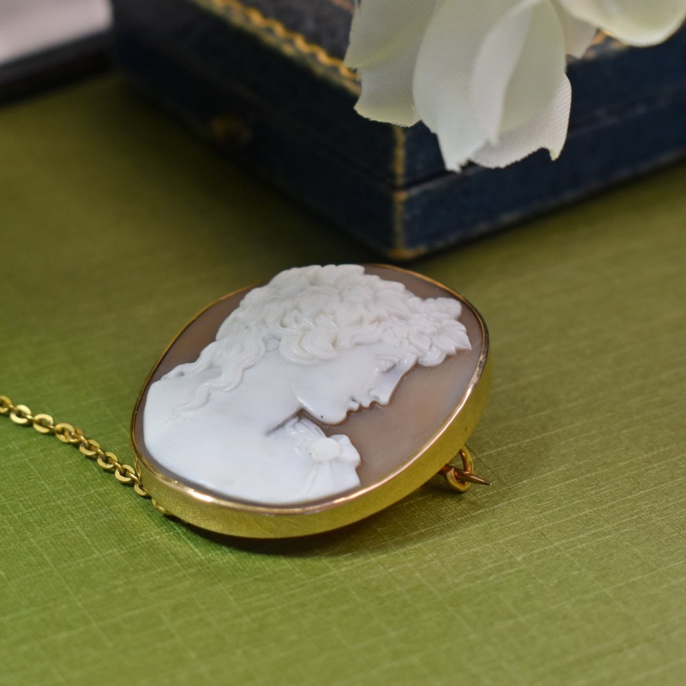 An oval Victorian shell cameo brooch depicting a relief profile carving of Antinous adorned with a floral wreath, set in a gold frame. View IV
