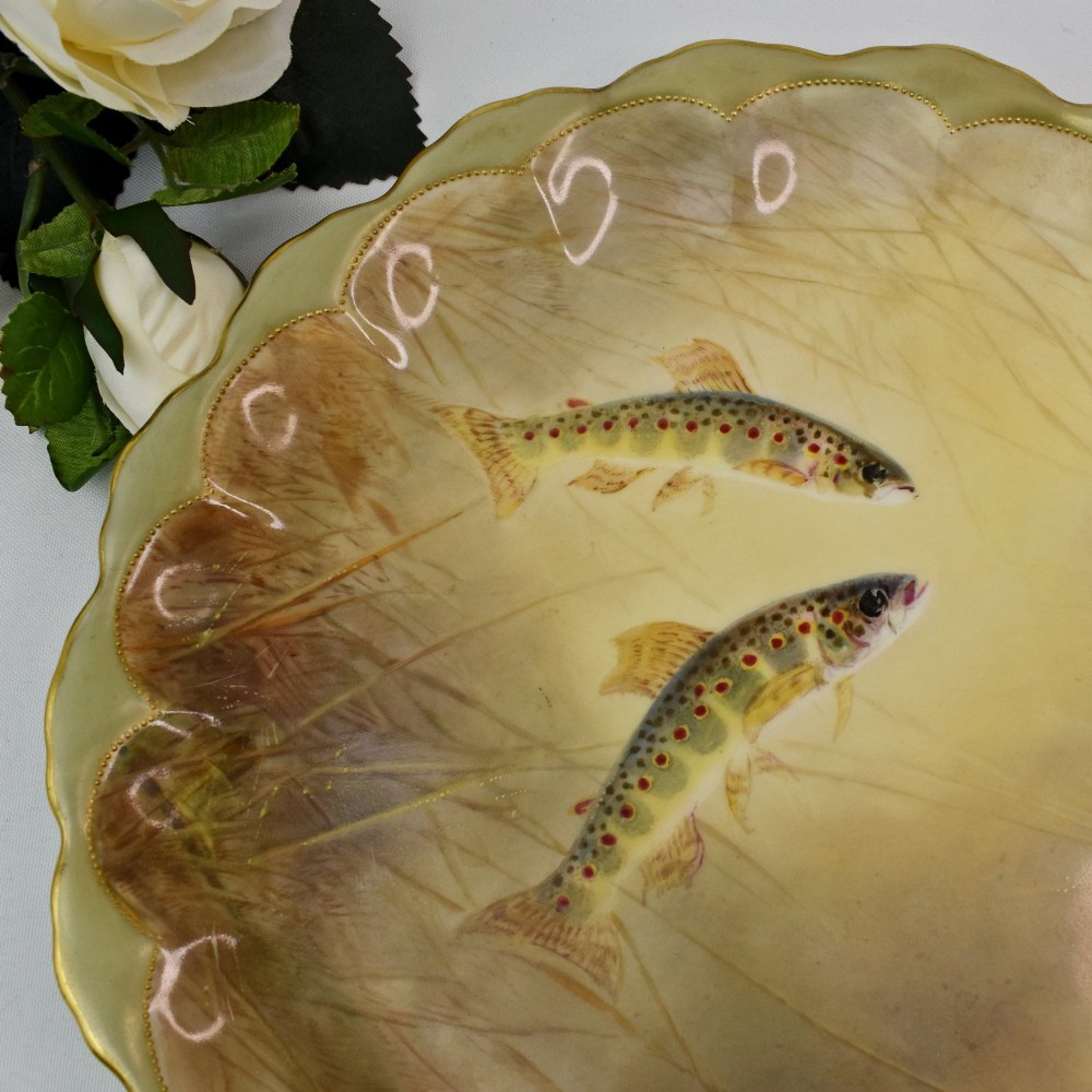 A set of four circular porcelain cabinet plates with scalloped gold rims, each featuring a central hand-painted scene of fish swimming in natural river settings. View VI