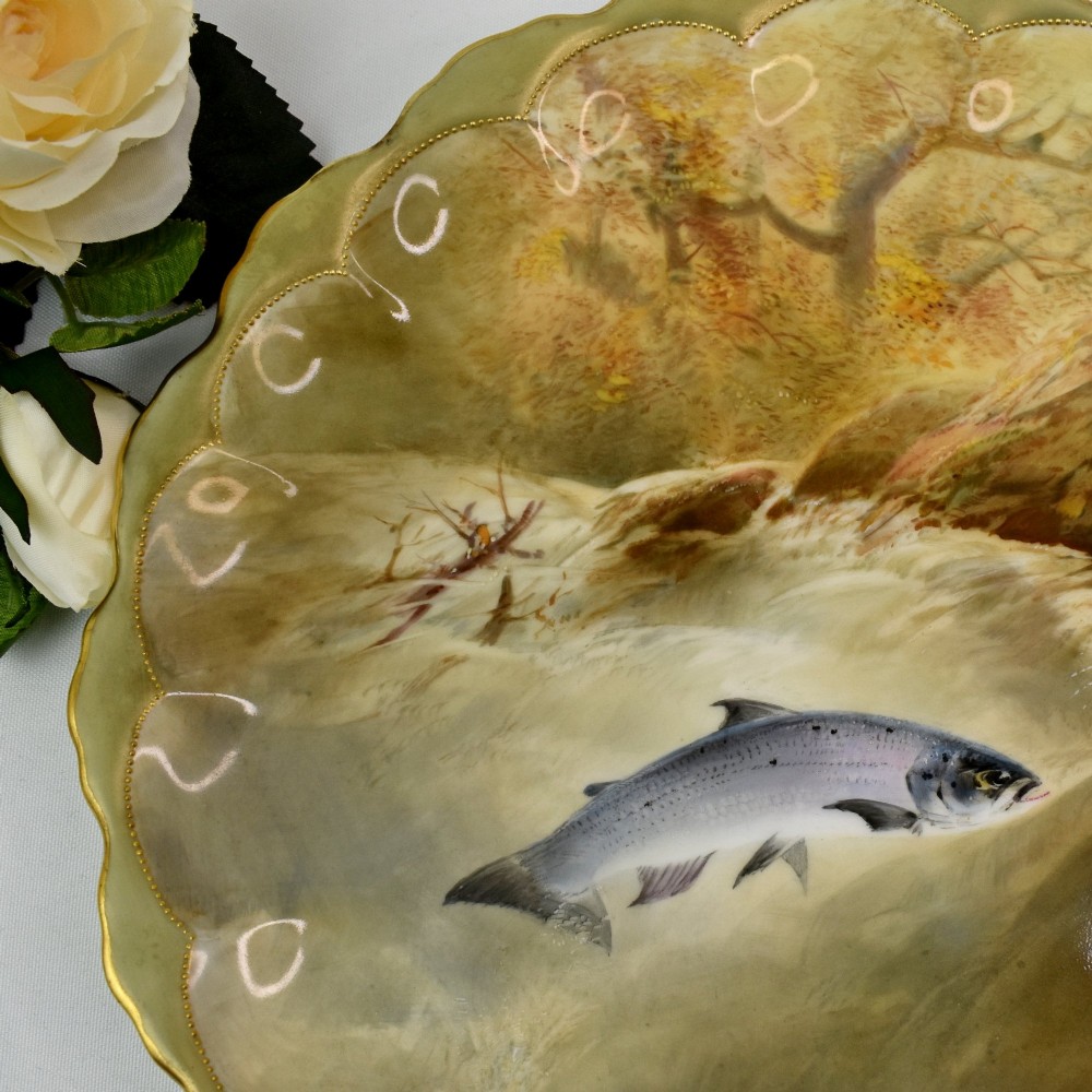 A set of four circular porcelain cabinet plates with scalloped gold rims, each featuring a central hand-painted scene of fish swimming in natural river settings. View VII