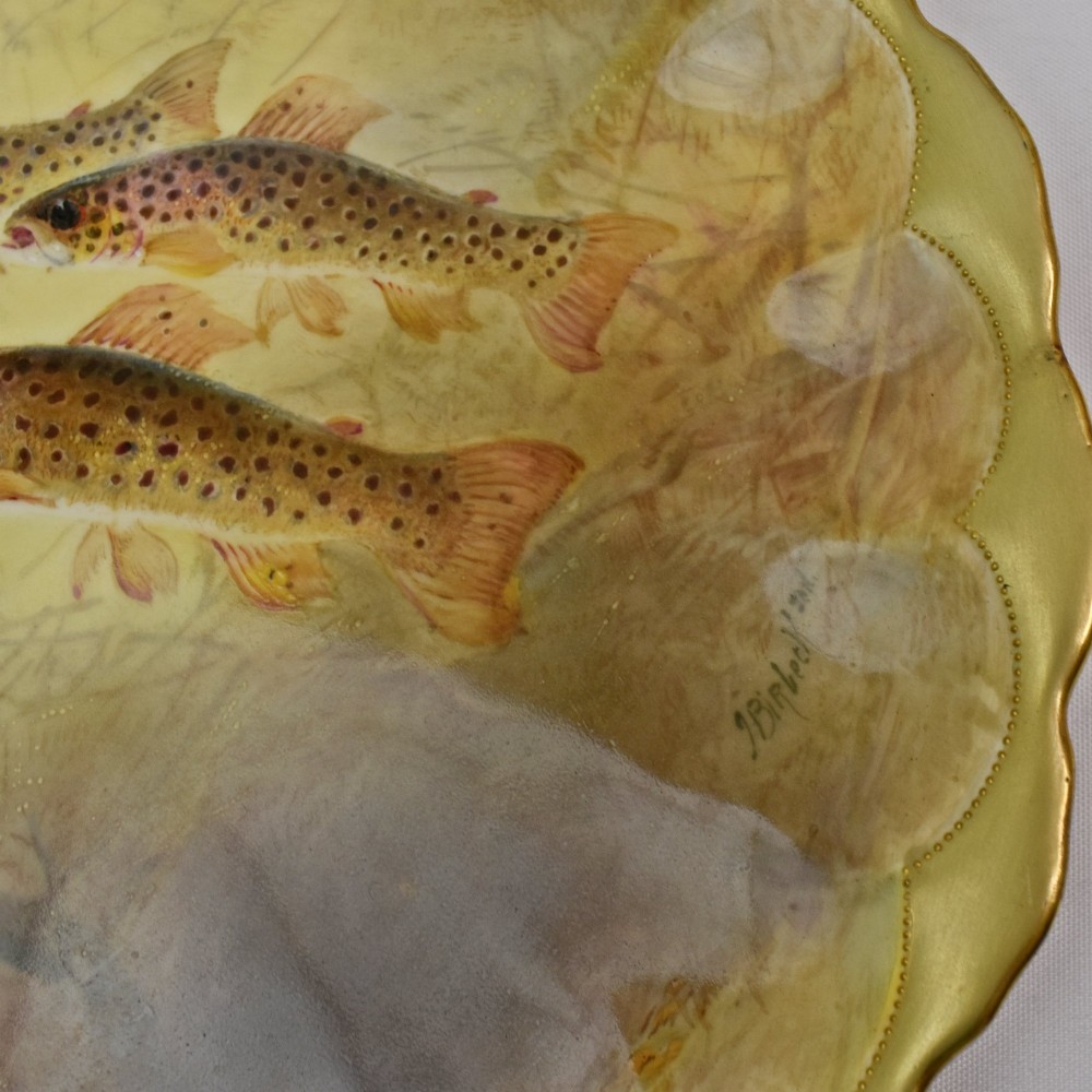 A set of four circular porcelain cabinet plates with scalloped gold rims, each featuring a central hand-painted scene of fish swimming in natural river settings. View IX