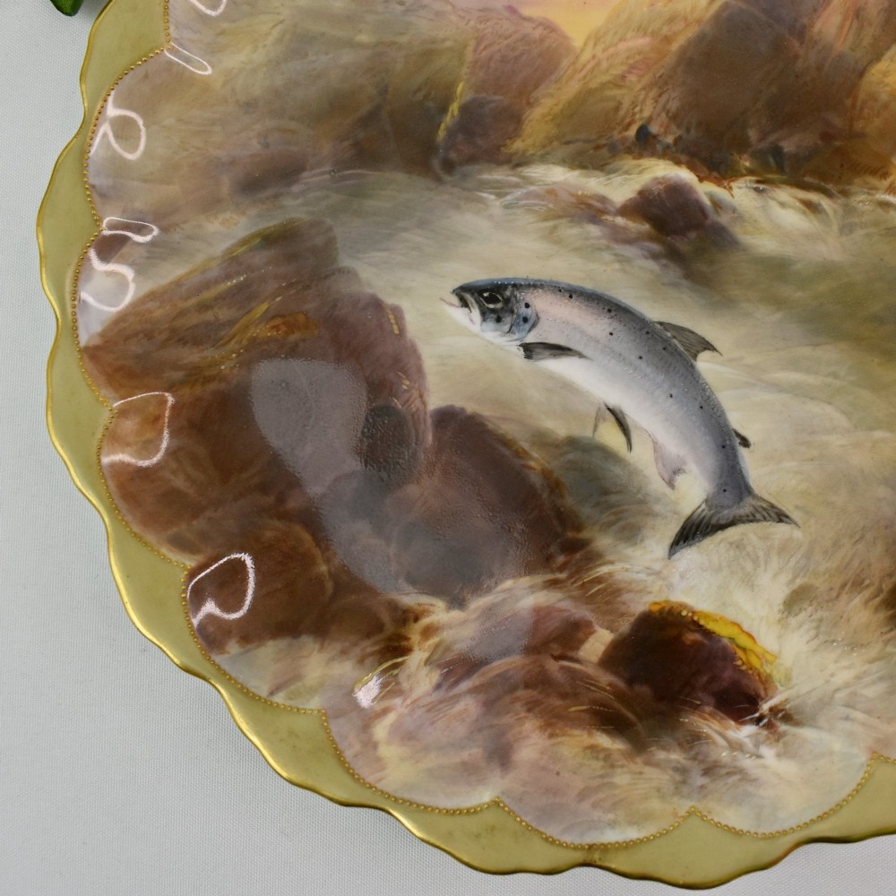 A set of four circular porcelain cabinet plates with scalloped gold rims, each featuring a central hand-painted scene of fish swimming in natural river settings. View X