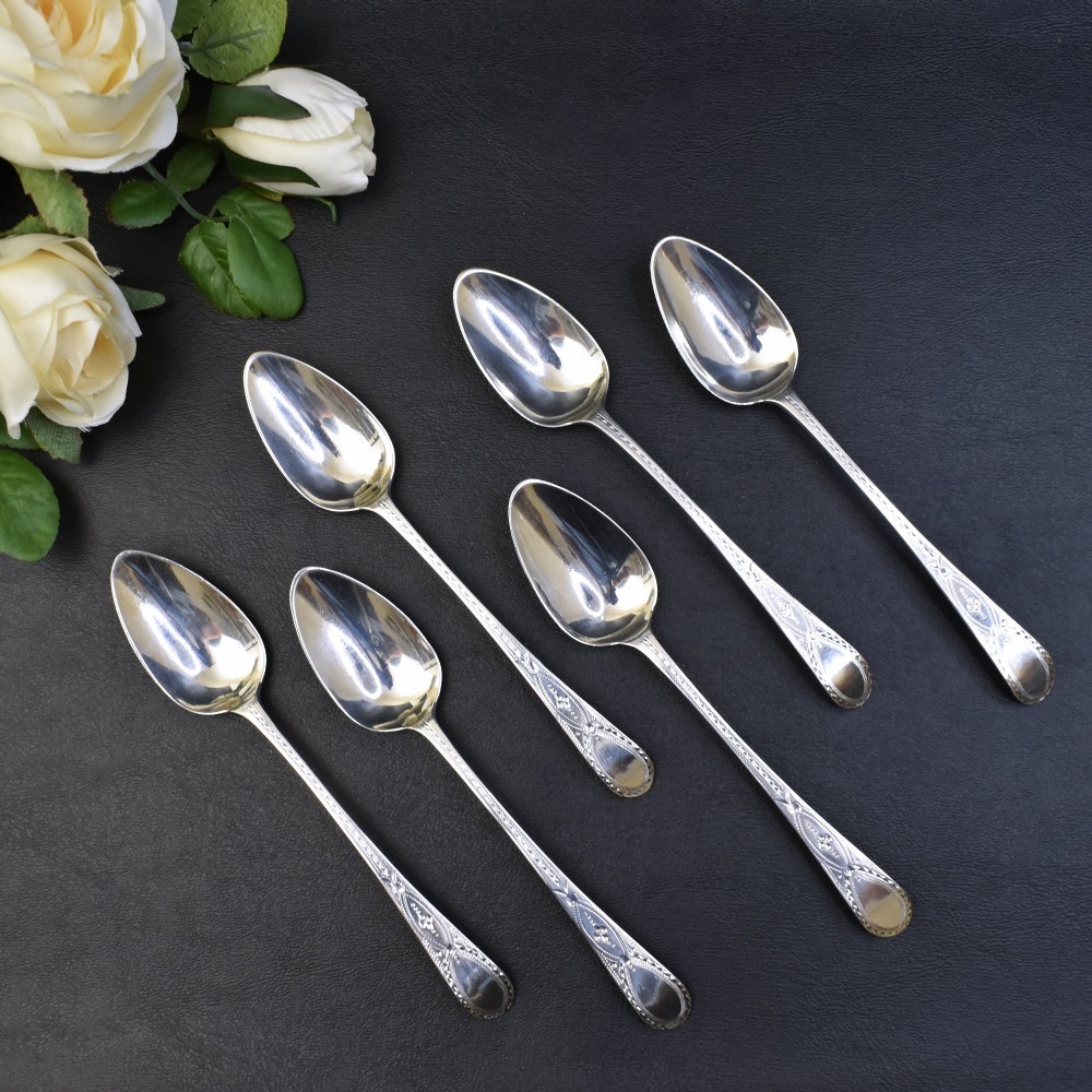 A set of six George III sterling silver teaspoons featuring bright-cut engraved stems and smooth oval bowls.