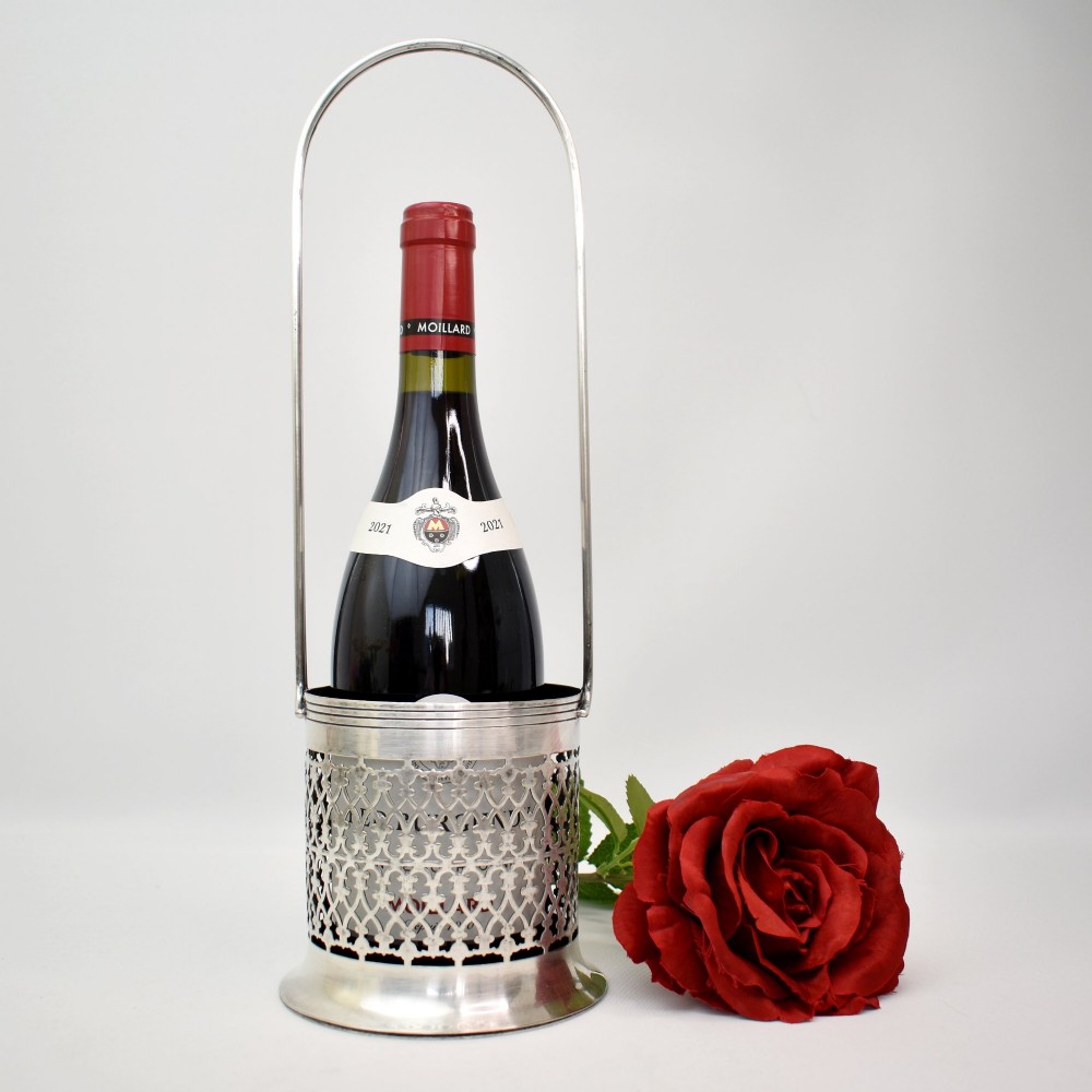 An early 20th-century silver-plated bottle holder featuring pierced geometric lattice fretwork, a flared base, and an upright twin handle. View II