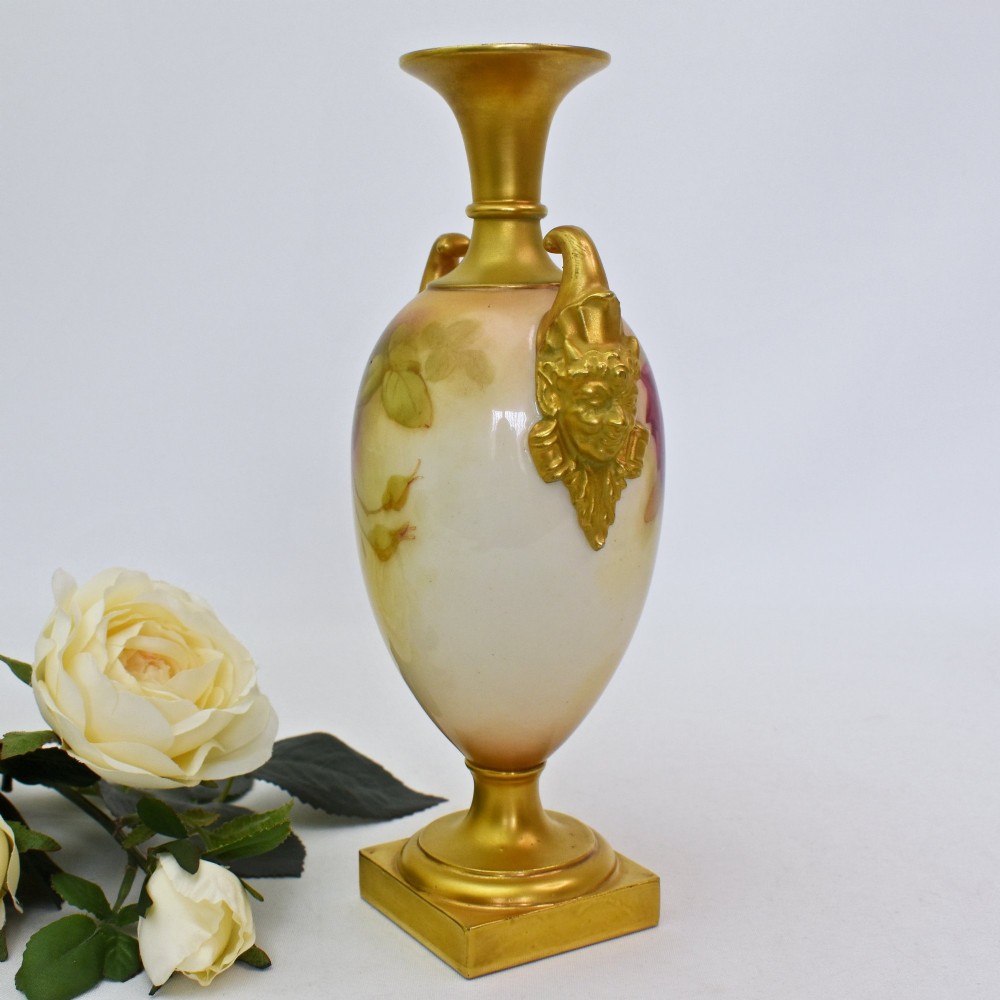 A hand-painted Royal Worcester porcelain vase decorated with pink and red roses, featuring gilded jester mask handles and a square base. View IV