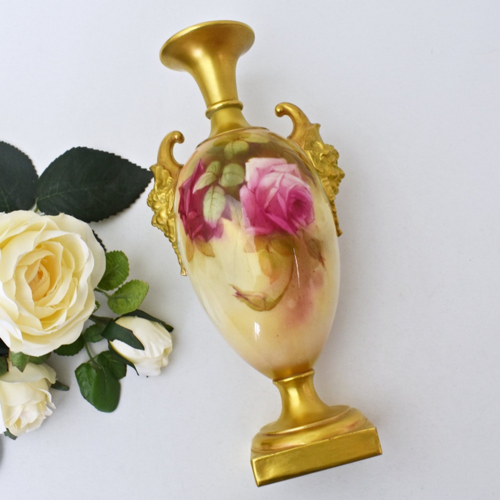 A hand-painted Royal Worcester porcelain vase decorated with pink and red roses, featuring gilded jester mask handles and a square base. View V