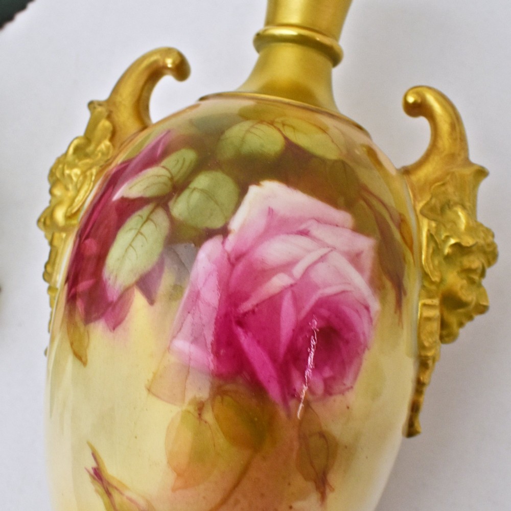 A hand-painted Royal Worcester porcelain vase decorated with pink and red roses, featuring gilded jester mask handles and a square base. View VI