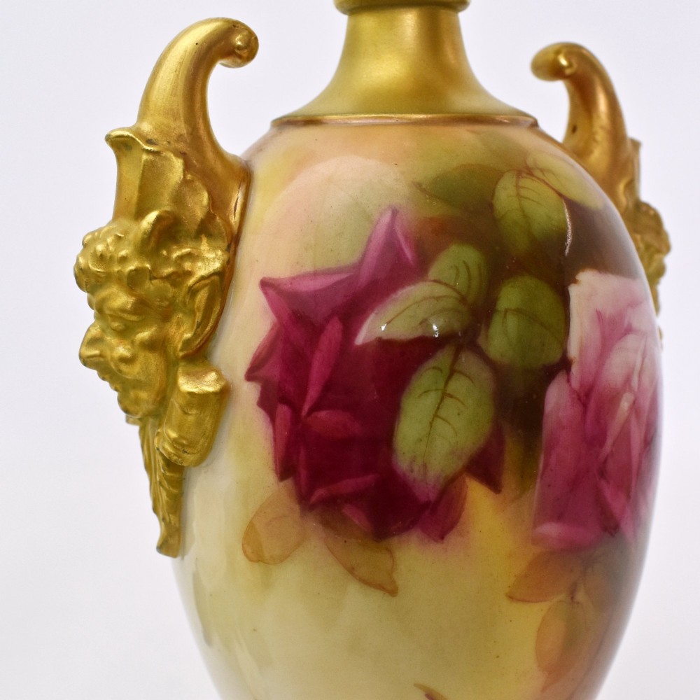 A hand-painted Royal Worcester porcelain vase decorated with pink and red roses, featuring gilded jester mask handles and a square base. View VII