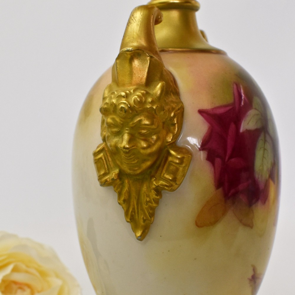 A hand-painted Royal Worcester porcelain vase decorated with pink and red roses, featuring gilded jester mask handles and a square base. View IX