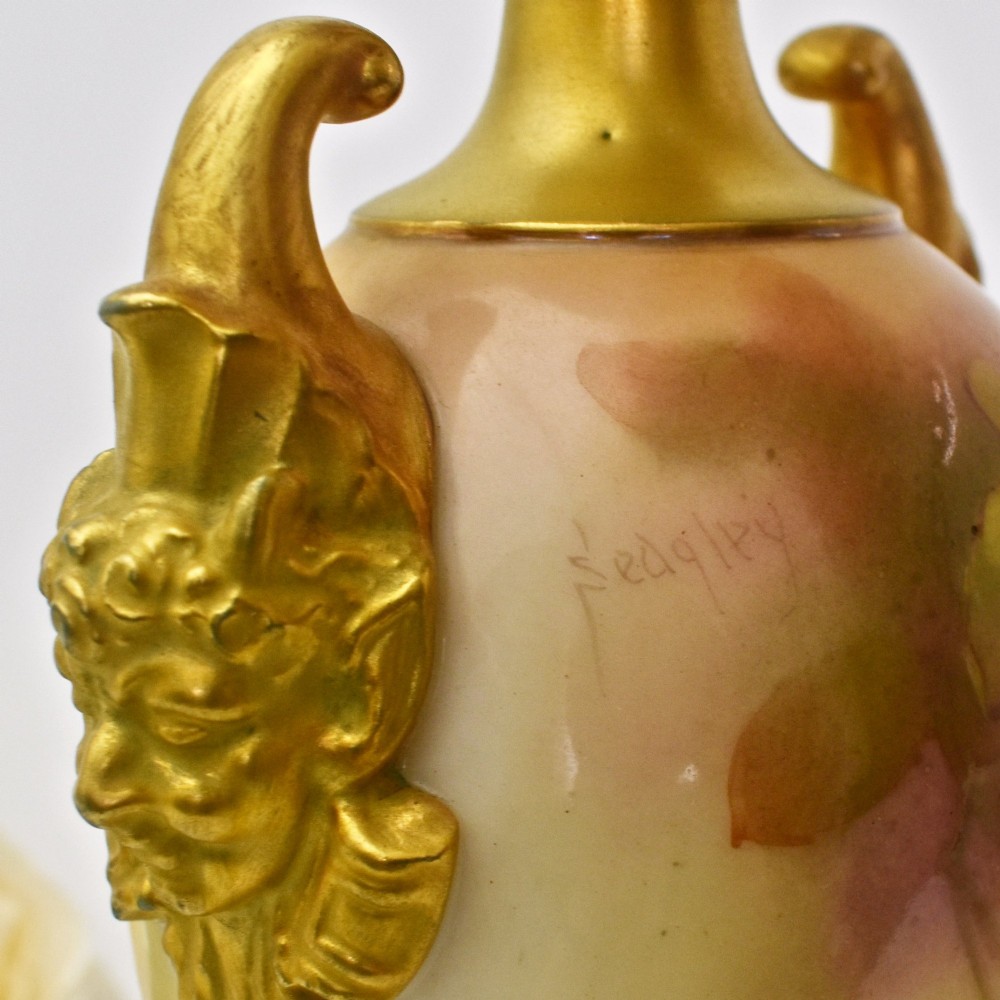 A hand-painted Royal Worcester porcelain vase decorated with pink and red roses, featuring gilded jester mask handles and a square base. View X