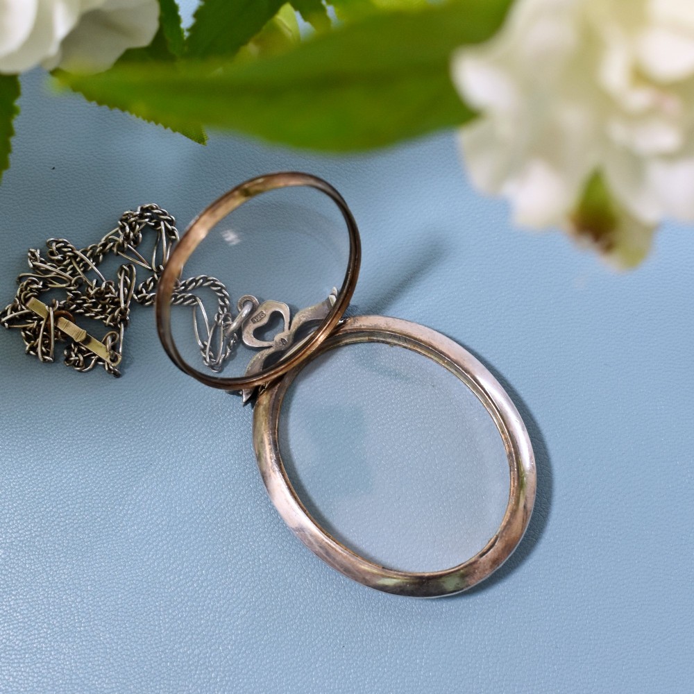 An oval glass portrait locket framed by a border of paste stones and topped with a silver ribbon bow motif on a chain. View VI
