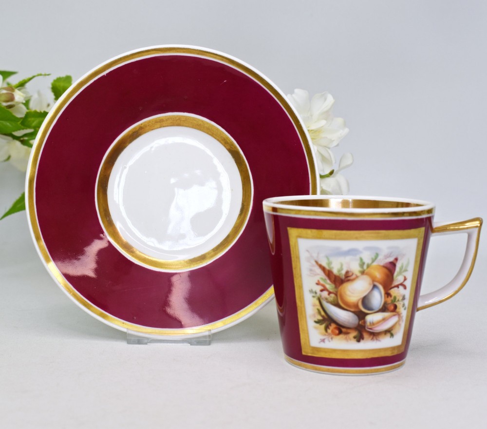 A Regency-era porcelain coffee cup and saucer featuring a deep claret ground, gilded borders, and a hand-painted panel depicting seashells. View II