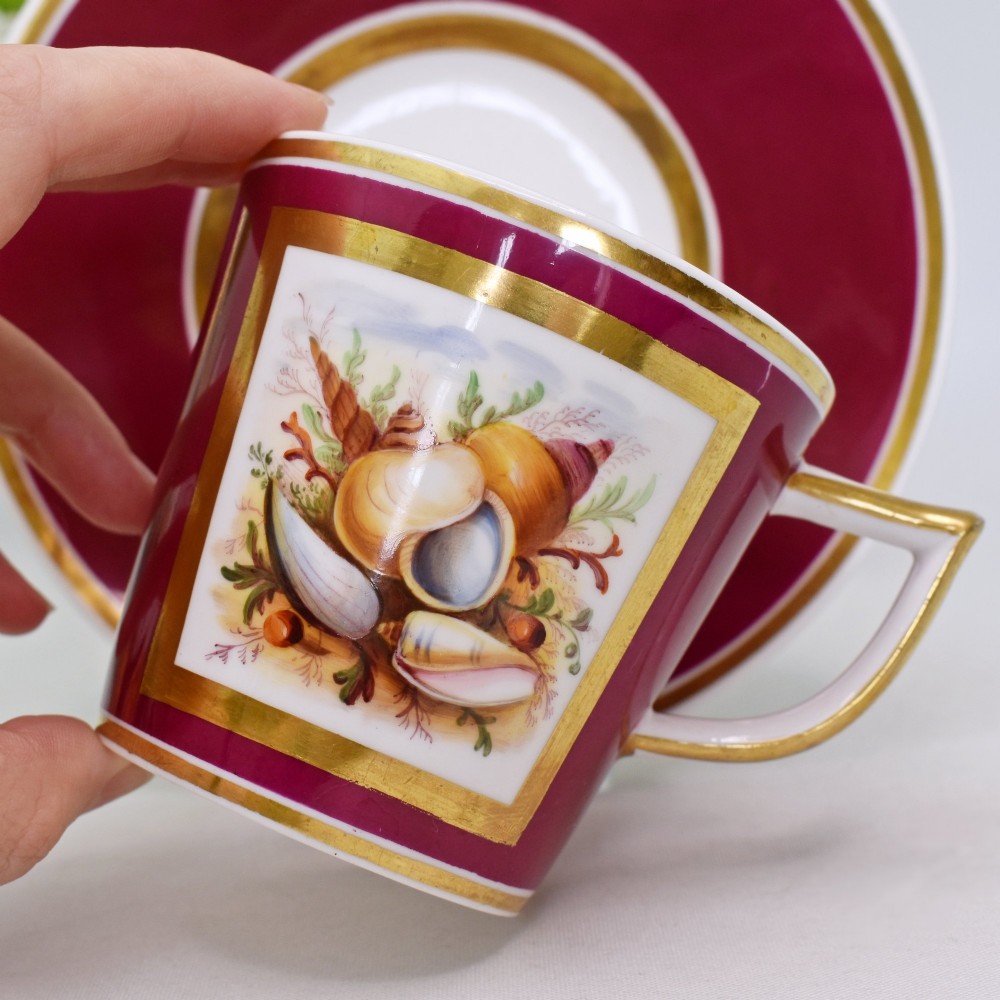 A Regency-era porcelain coffee cup and saucer featuring a deep claret ground, gilded borders, and a hand-painted panel depicting seashells. View III