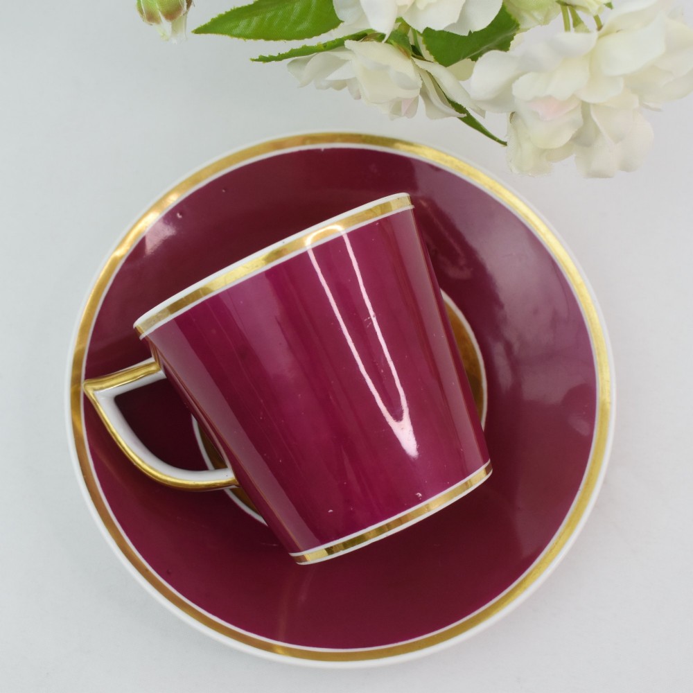 A Regency-era porcelain coffee cup and saucer featuring a deep claret ground, gilded borders, and a hand-painted panel depicting seashells. View VI