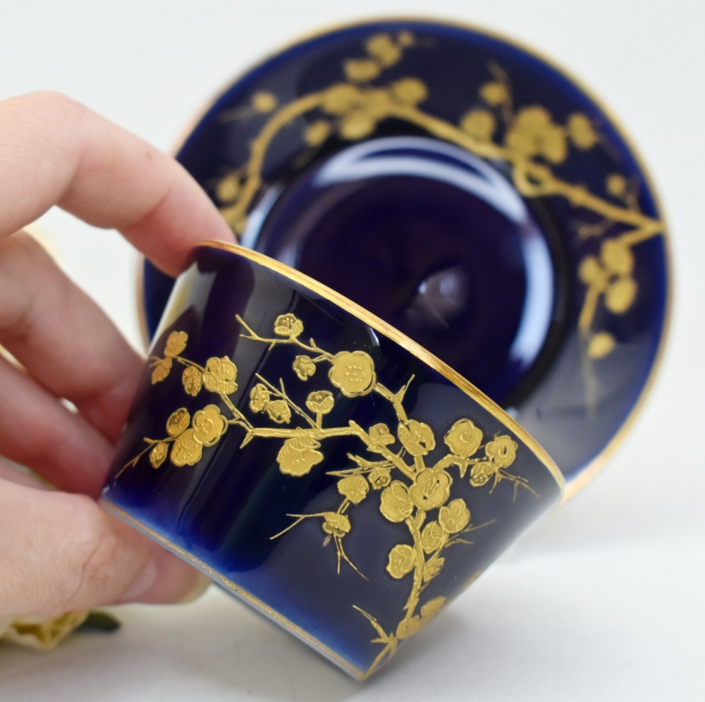 A dark cobalt blue porcelain coffee cup and matching saucer decorated with raised gilt floral branches, a perched bird, and a bamboo-style handle. View III
