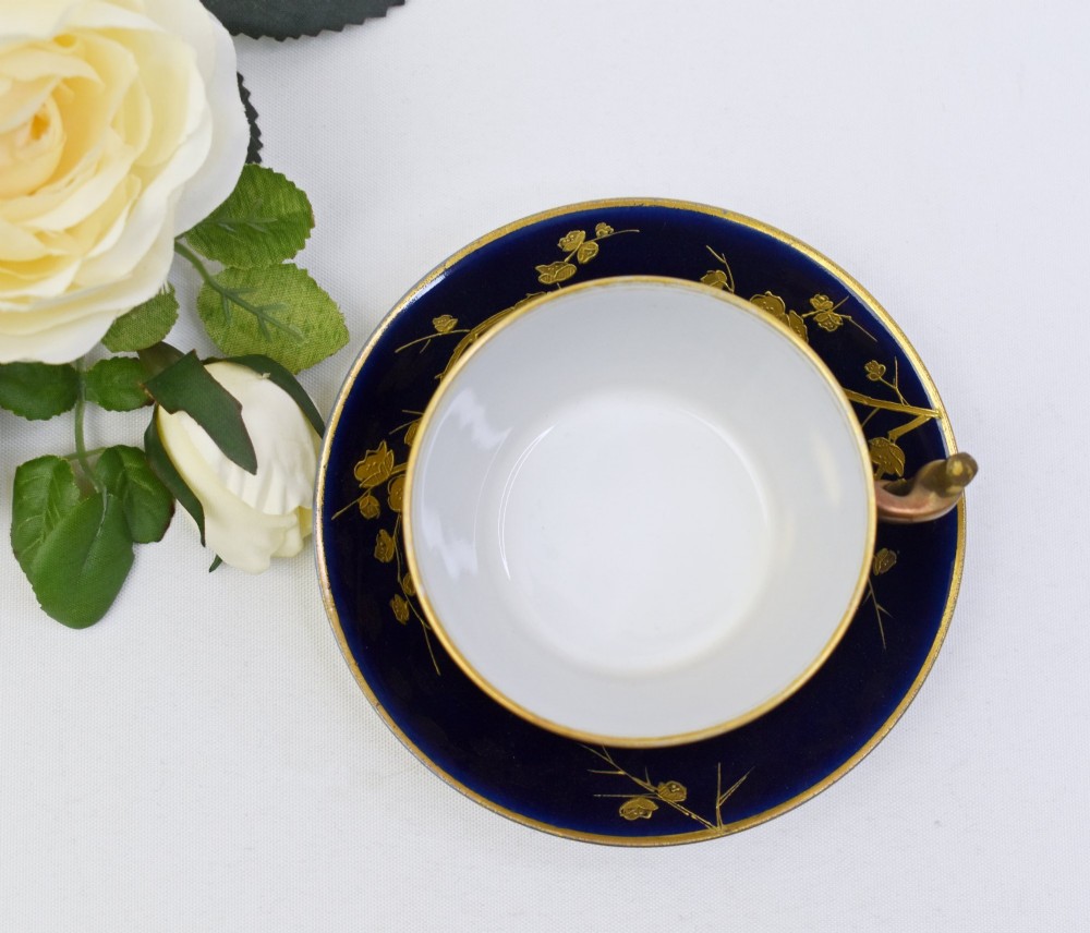 A dark cobalt blue porcelain coffee cup and matching saucer decorated with raised gilt floral branches, a perched bird, and a bamboo-style handle. View IV
