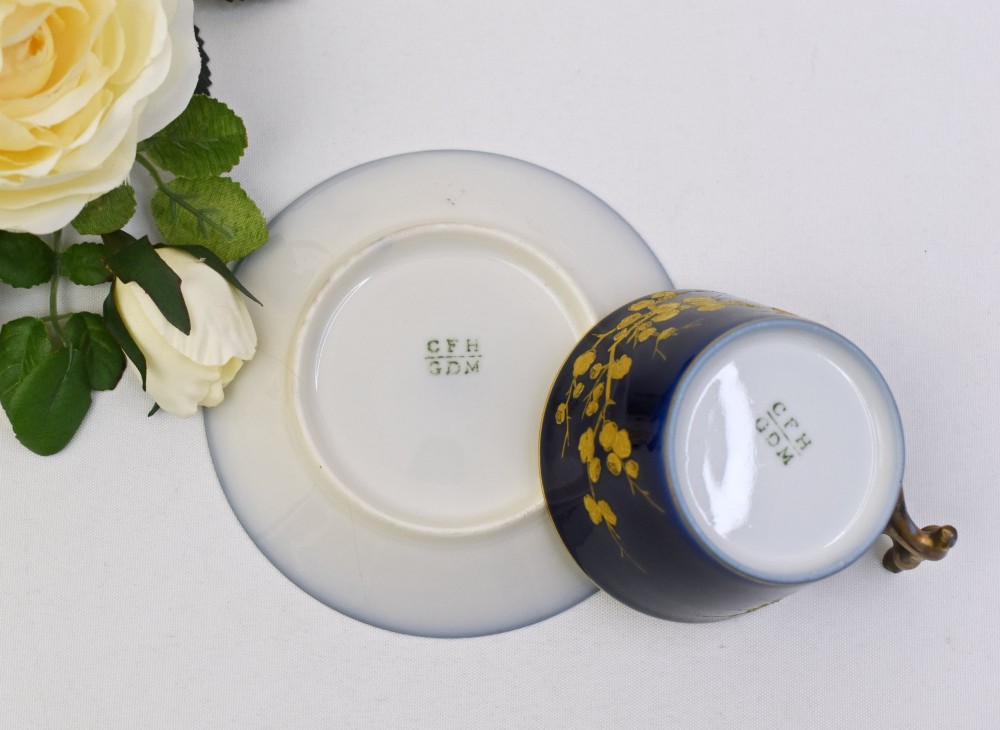 A dark cobalt blue porcelain coffee cup and matching saucer decorated with raised gilt floral branches, a perched bird, and a bamboo-style handle. View V