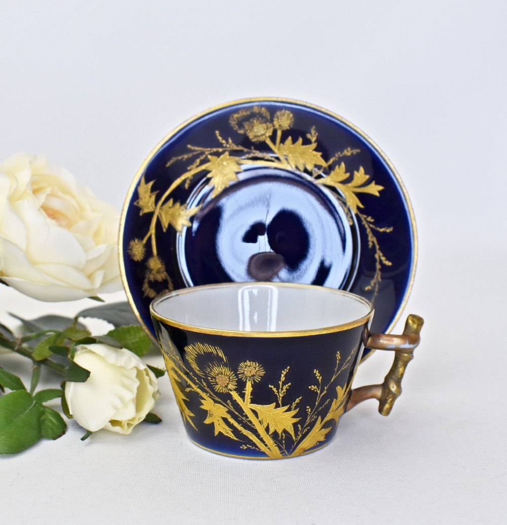 A French porcelain coffee cup and saucer in deep cobalt blue with raised gold gilded thistle motifs and a branch-formed gilt handle.