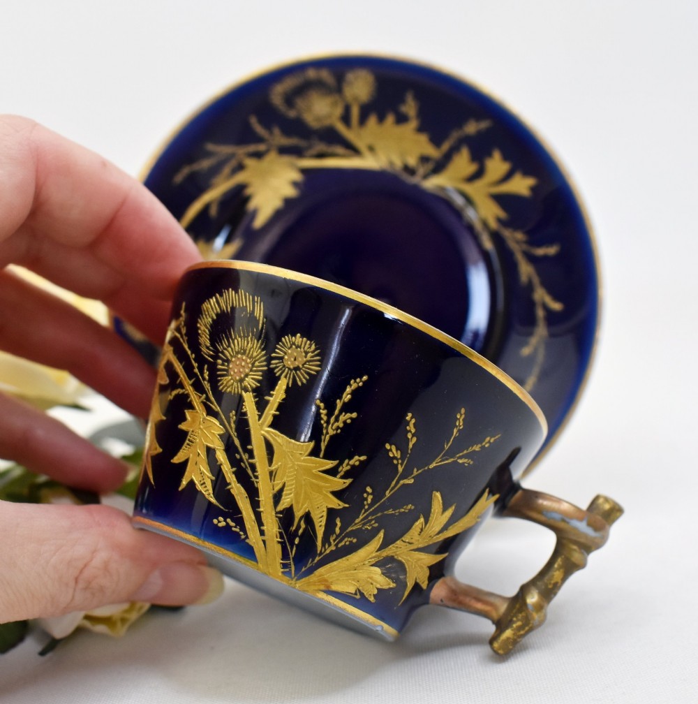 A French porcelain coffee cup and saucer in deep cobalt blue with raised gold gilded thistle motifs and a branch-formed gilt handle. View II
