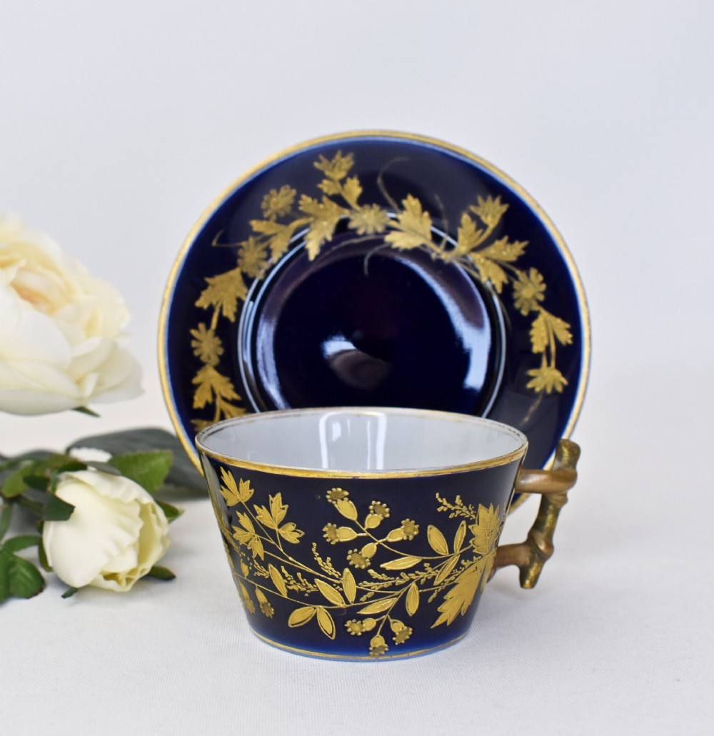 A cobalt blue French porcelain coffee cup and matching saucer decorated with raised gilt floral motifs and a faux-twig gilded handle.
