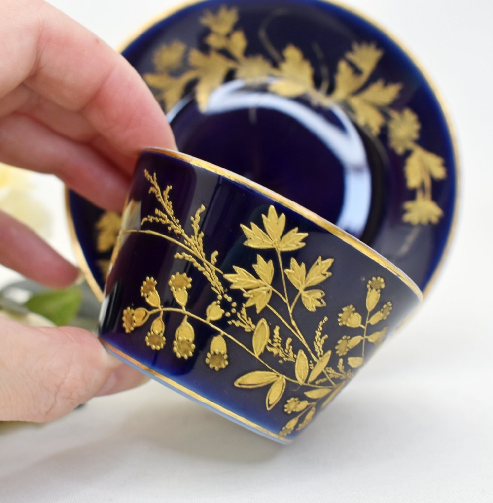 A cobalt blue French porcelain coffee cup and matching saucer decorated with raised gilt floral motifs and a faux-twig gilded handle. View II