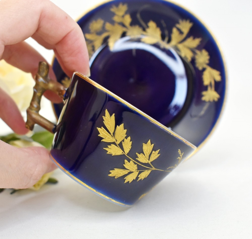 A cobalt blue French porcelain coffee cup and matching saucer decorated with raised gilt floral motifs and a faux-twig gilded handle. View III