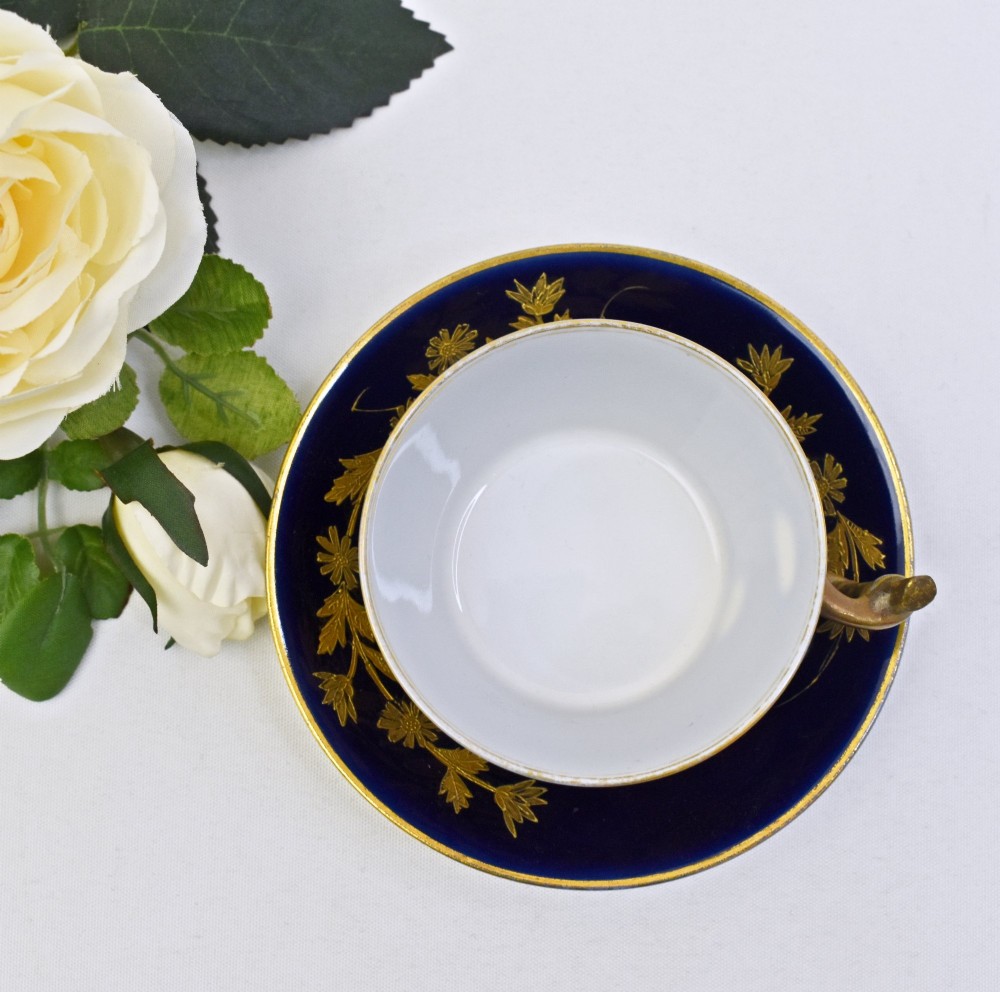 A cobalt blue French porcelain coffee cup and matching saucer decorated with raised gilt floral motifs and a faux-twig gilded handle. View IV