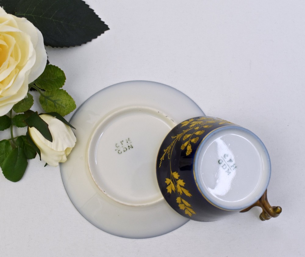 A cobalt blue French porcelain coffee cup and matching saucer decorated with raised gilt floral motifs and a faux-twig gilded handle. View V