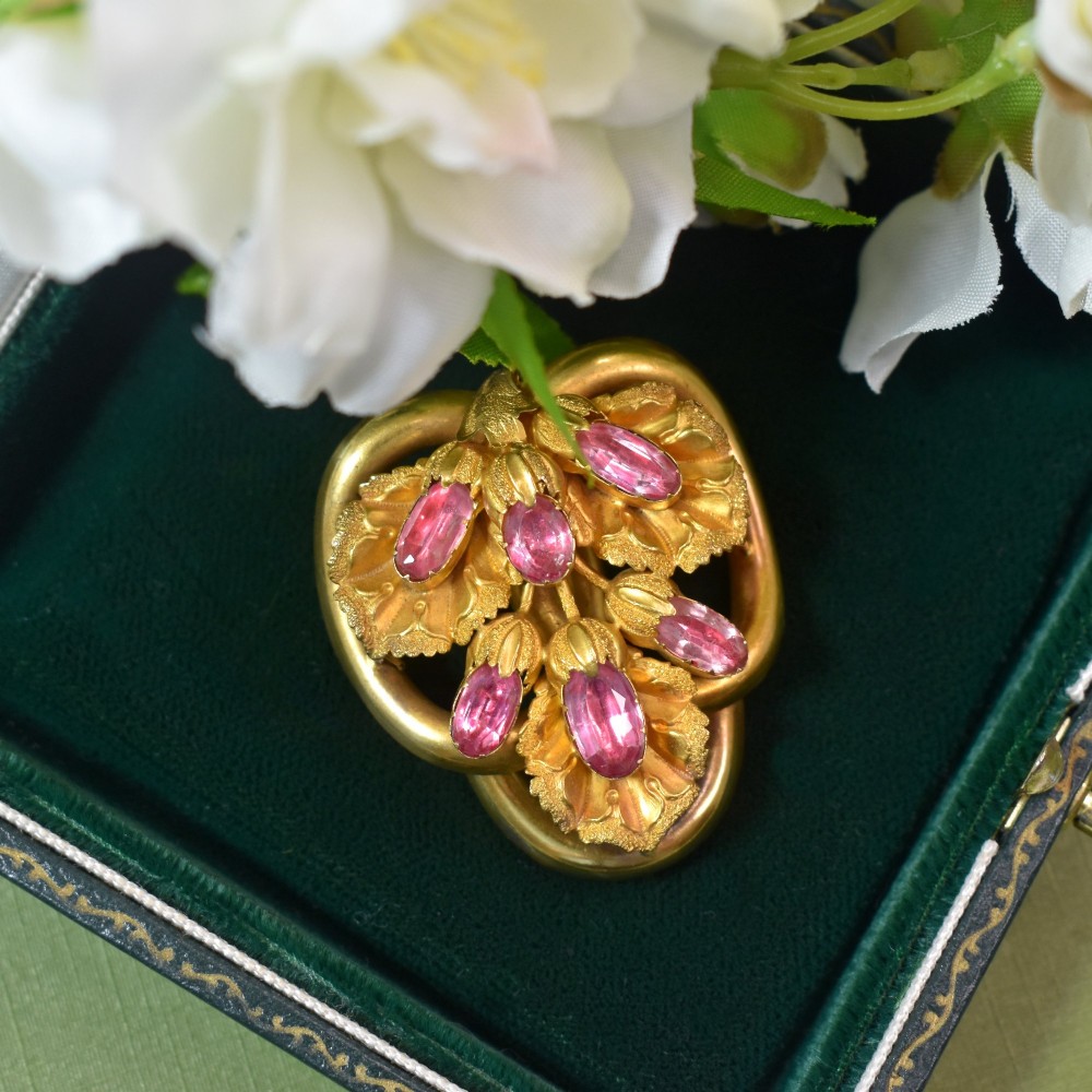 An early Victorian 15ct gold floral brooch featuring oval foil-backed pink topaz gemstones set amongst chased gold leaf and scroll motifs.