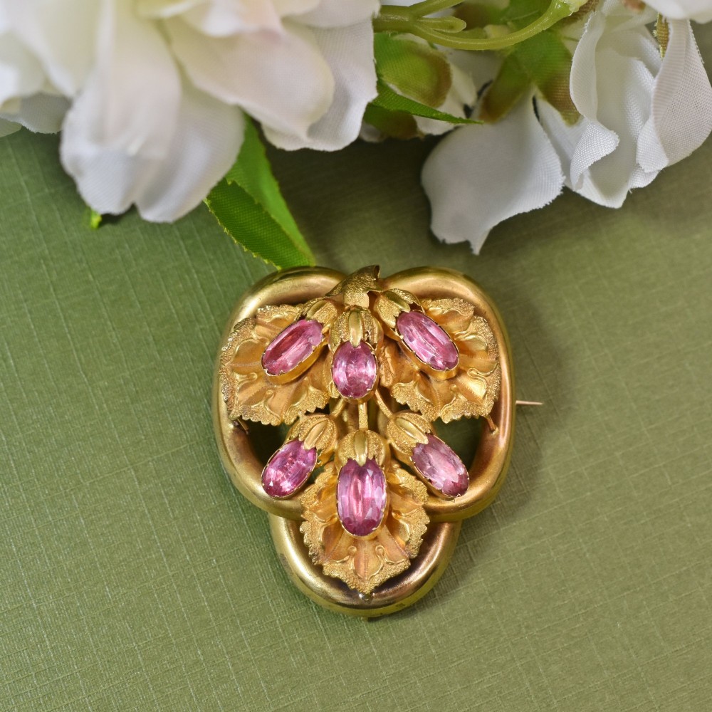 An early Victorian 15ct gold floral brooch featuring oval foil-backed pink topaz gemstones set amongst chased gold leaf and scroll motifs. View II